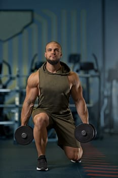 Sportive man workout with dumbbells doing lunges. Photo of young man with good physique isolated on gym. Strength and motivation.