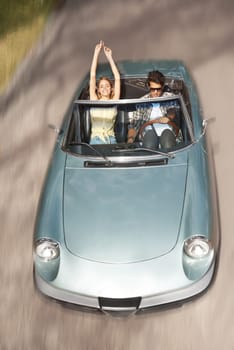 Feeling the rushing air. High angle shot of a young woman with her arms raised while riding in a convertible with her boyfriend