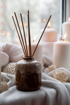 Aroma reed diffuser. Bottle container with wood stick diffusers Essential oils to scent your home fragnance concept autumn holidays at cozy home on the windowsill Hygge aesthetic atmosphere on knitted white sweater. Still life of micro moment candid slow living. Mental health wellbeing exercises Raining Outside