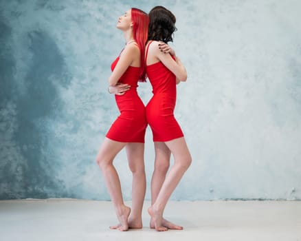 A full-length portrait of two women dressed in identical red dresses and standing back to back. Lesbian intimacy