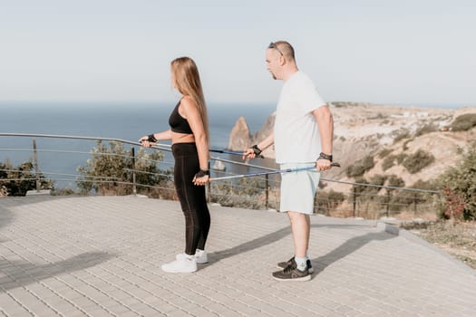 Happy Middle aged couple or friends practicing nordic walking in park near sea. Mature couple with trekking poles walking, practicing Nordic walking outdoors. Aging youthfully and sport concept.