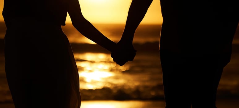 Silhouette, couple and holding hands at sunset on beach for vacation or holiday outdoor. Behind man and woman in nature with creative art, space and ocean for love, shadow and travel or freedom.