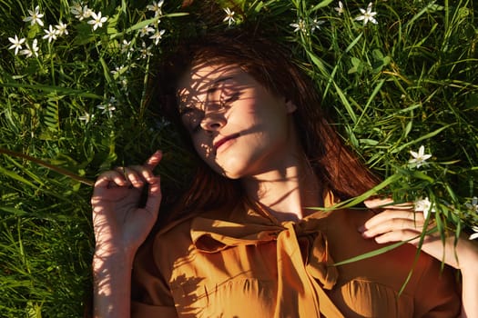 a relaxed woman, resting lying in the green grass, in a long orange dress, with her eyes closed and a pleasant smile on her face, recuperating, illuminated by the warm rays of the setting summer sun. High quality photo