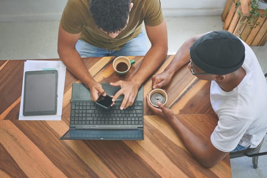 Technology and coffee are the foundation of modern business. High angle shot of two unrecognizable friends sitting together and using technology during a discussion in a coffeeshop