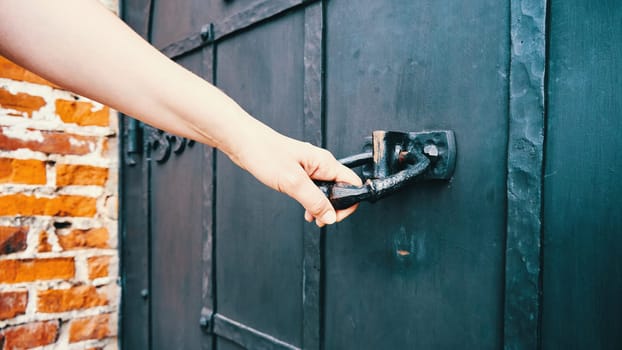 Woman's hand trying to open an old black wooden door