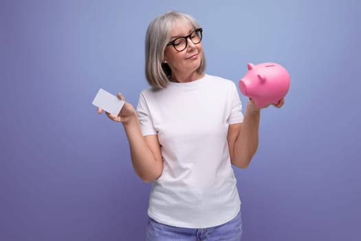 a woman of mature years with gray hair holds money capital from a piggy bank on a studio background with copy space.