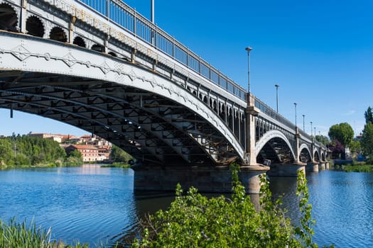 Perspective view of the Enrique Estevan bridge over the Tormes river in the city of Salamanca, with blue sky.