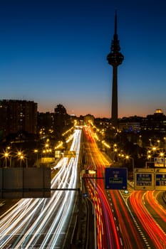 Sunset view of a Madrid skyline with the Torrespaña communications tower in the background and lines of traffic lights.