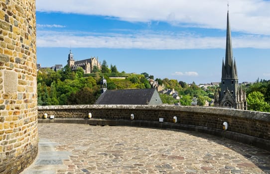View of the French town of Fougeres from the castle, with a background of blue sky and clouds at sunset and a church in the foreground.