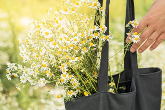 A black bag with a bouquet of daisies on field background.