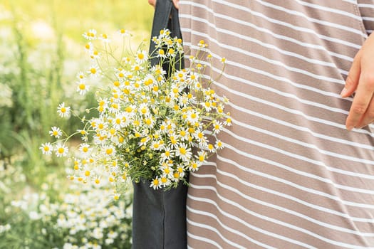 A black bag with a bouquet of daisies on field background.