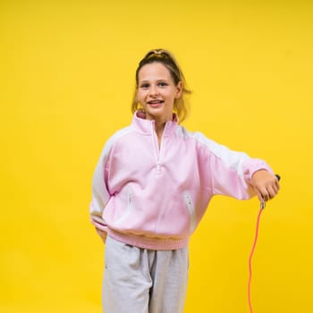 Beautiful sportsgirl with skipping rope isolated on a yellow studio