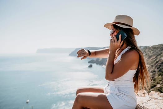 Successful business woman in yellow hat working on laptop by the sea. Pretty lady typing on computer at summer day outdoors. Freelance, travel and holidays concept.