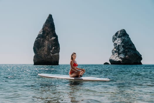 Close up shot of beautiful young caucasian woman with black hair and freckles looking at camera and smiling. Cute woman portrait in a pink bikini posing on a volcanic rock high above the sea