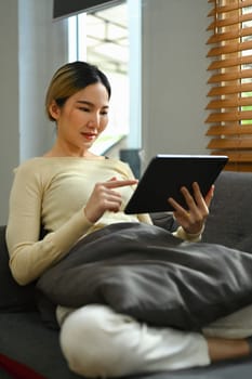 Casual millennial woman sitting on couch and using digital tablet. Technology, people and lifestyle concept.