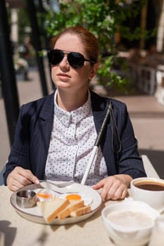 A blind woman in a business suit eats scrambled eggs in a street cafe