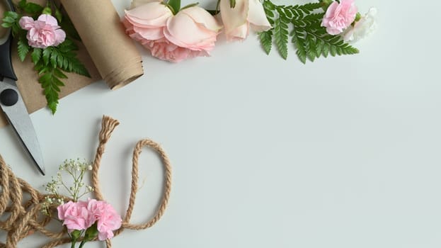 Florist workspace. Pink flowers, shears, wrapping paper and leaves arrangement on white background with copy space.