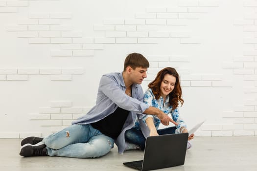 Couple Use Laptop Computer, while Sitting on the Living Floor room of their Apartment. Boyfriend and Girlfriend Talk, Shop on Internet, Choose Product to Order Online, Watch Streaming Service