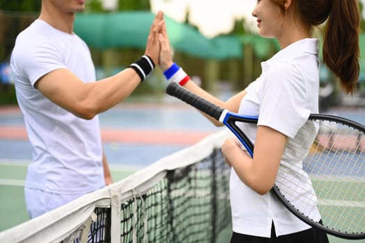 Shot of two young tennis players giving each other high five over net at tennis court.