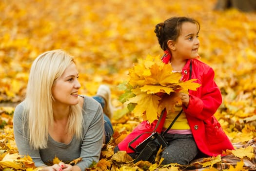 Young mother playing with her daughter in autumn park.