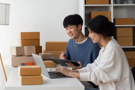 Happy couple people packing parcel boxes, couple lover checking order online on laptop at home.
