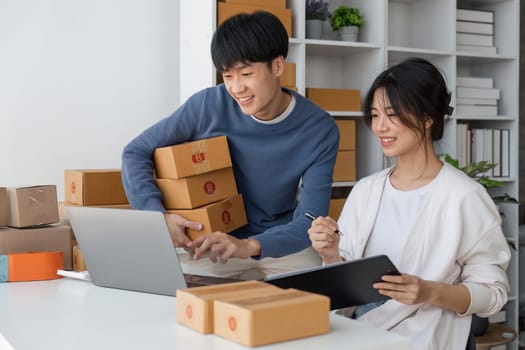 Happy couple people packing parcel boxes, couple lover checking order online on laptop at home.