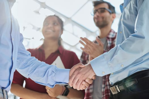 Young startup in casual clothes shaking hands in a modern office space by the window.