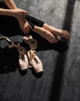 Faceless ballerina sits on the floor and puts on pointe shoes