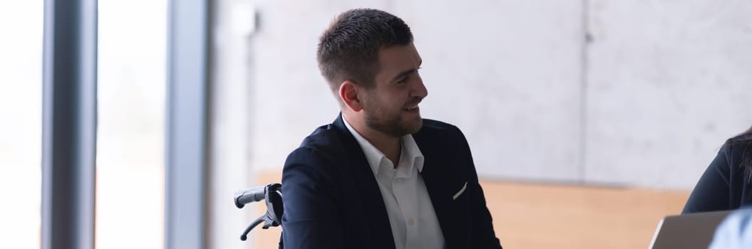 Wide crop photo of wheelchair bound businessman confidently leads a business meeting in a large, modern office, exemplifying inclusive leadership, effective communication, and the power of diversity in driving success and achieving impactful results