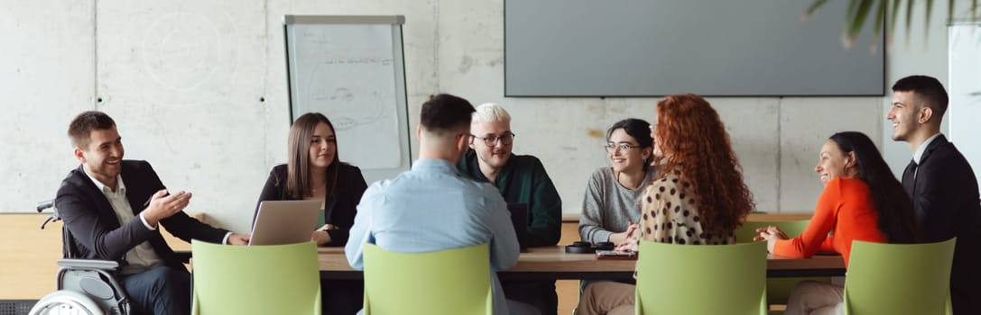 Wide crop photo of a diverse group of business professionals, including an person with a disability, gathered at a modern office for a productive and inclusive meeting