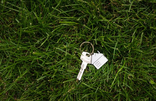 Keychain in the form of a house on the background of a green lawn. The concept of buying a home, apartment, cottage, house. Real estate in an ecologically clean area, a place for an inscription