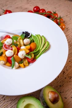 top view salad with avacado, mozzarella and tomatoes in a white plate.