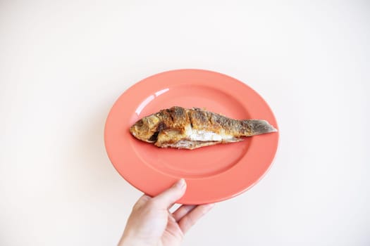 A whole fried carp with a fried crust, served on a bright red plate. A hand holds a plate on a white background