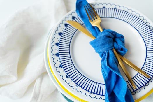 Serving design. Gold cutlery is tied with a blue napkin, on which the plates are on a green-yellow linen napkin