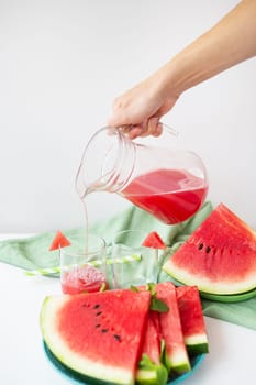 Close-up of fresh watermelon juice or smoothie in glasses with watermelon slices on a white table. A refreshing summer drink is poured into glasses