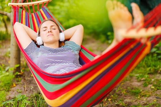 Young woman in headphones listening to music while resting in hammock outdoors.