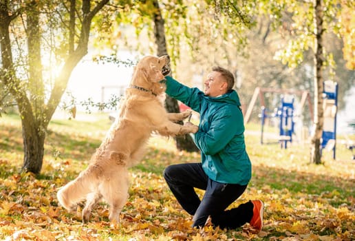 Man playing with his dog golden retriever in autumn park