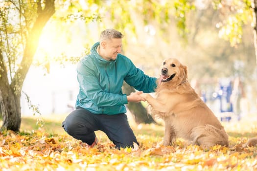 Man playing with his dog golden retriever in autumn park