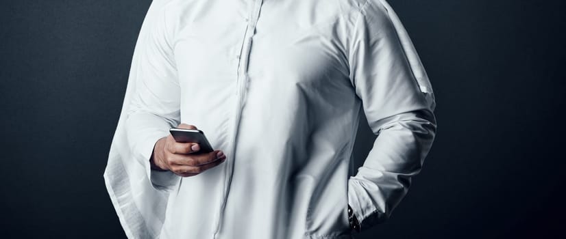 Accessing information for his work anywhere. Studio shot of an unrecognizable man dressed in Islamic traditional clothing posing against a dark background