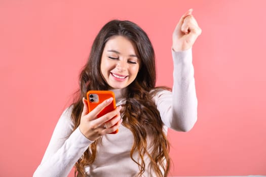 Long-haired lady with amused expression reads message on winning lottery on phone. Woman looks at won amount of money with shocking expression