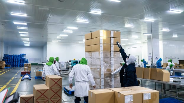 Unrecognizable Latino workers packing and securing cardboard boxes at a food production plant