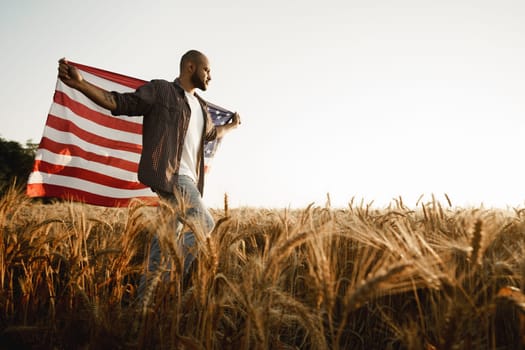 African american young man holding USA national flag through wheat field on dawn