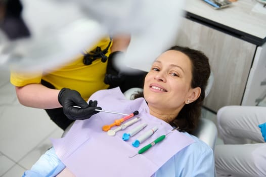 Pretty pregnant woman smiling looking at camera, sitting in dentist's chair with dental instruments and anesthetics on napkin on her chest. The concept of dental checkup and treatment during pregnancy
