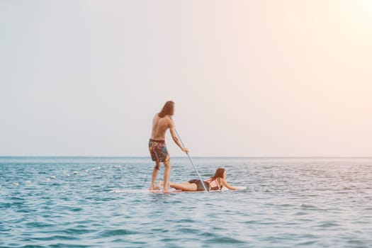 Silhouette of woman standing, surfing on SUP board, confident paddling through water surface. Idyllic sunset or sunrise. Sports active lifestyle at sea or river.