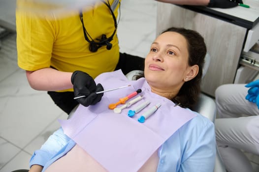 Close-up portrait of a multi ethnic beautiful pregnant woman lying on dentist's chair while a professional dentist treats and examines the oral cavity in a modern dental office. Dentistry. Pregnancy.