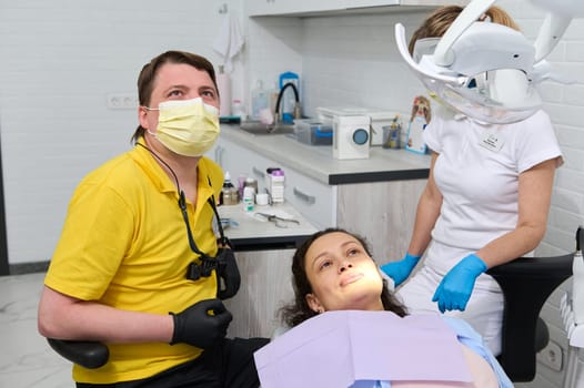 Professional male dental hygienist and a patient look at a screen broadcasting an x-ray image of the oral cavity and teeth. Happy young woman in dentist chair having dental checkup at dentistry clinic
