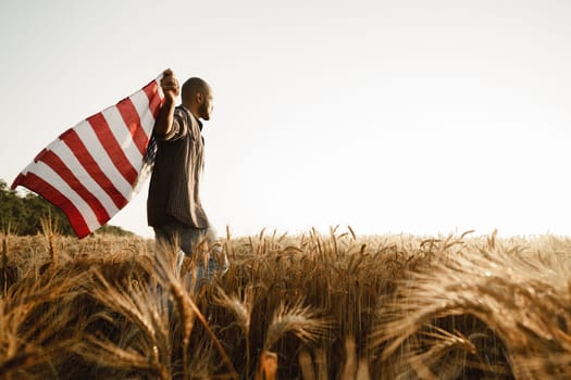 African american young man holding USA national flag through wheat field on dawn