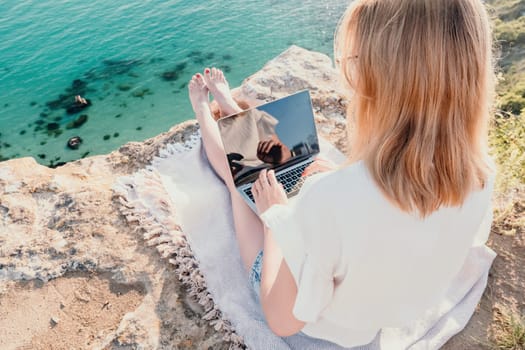 Woman sea laptop. Business woman in yellow hat working on laptop by sea. Close up on hands of pretty lady typing on computer outdoors summer day. Freelance, digital nomad, travel and holidays concept.