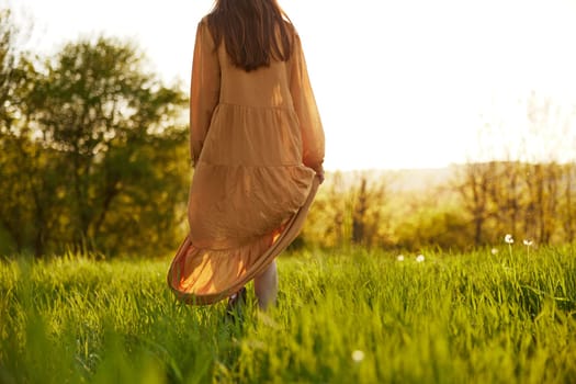a slender woman stands in a long orange dress with her back to the camera illuminated by the sunset rays of the sun and looks towards the sky. High quality photo