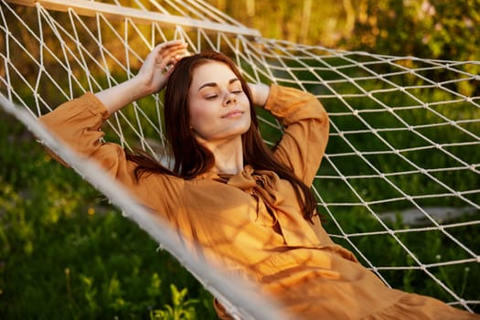 a happy woman is resting in a hammock with her eyes closed and her hands behind her head smiling happily enjoying the day. High quality photo